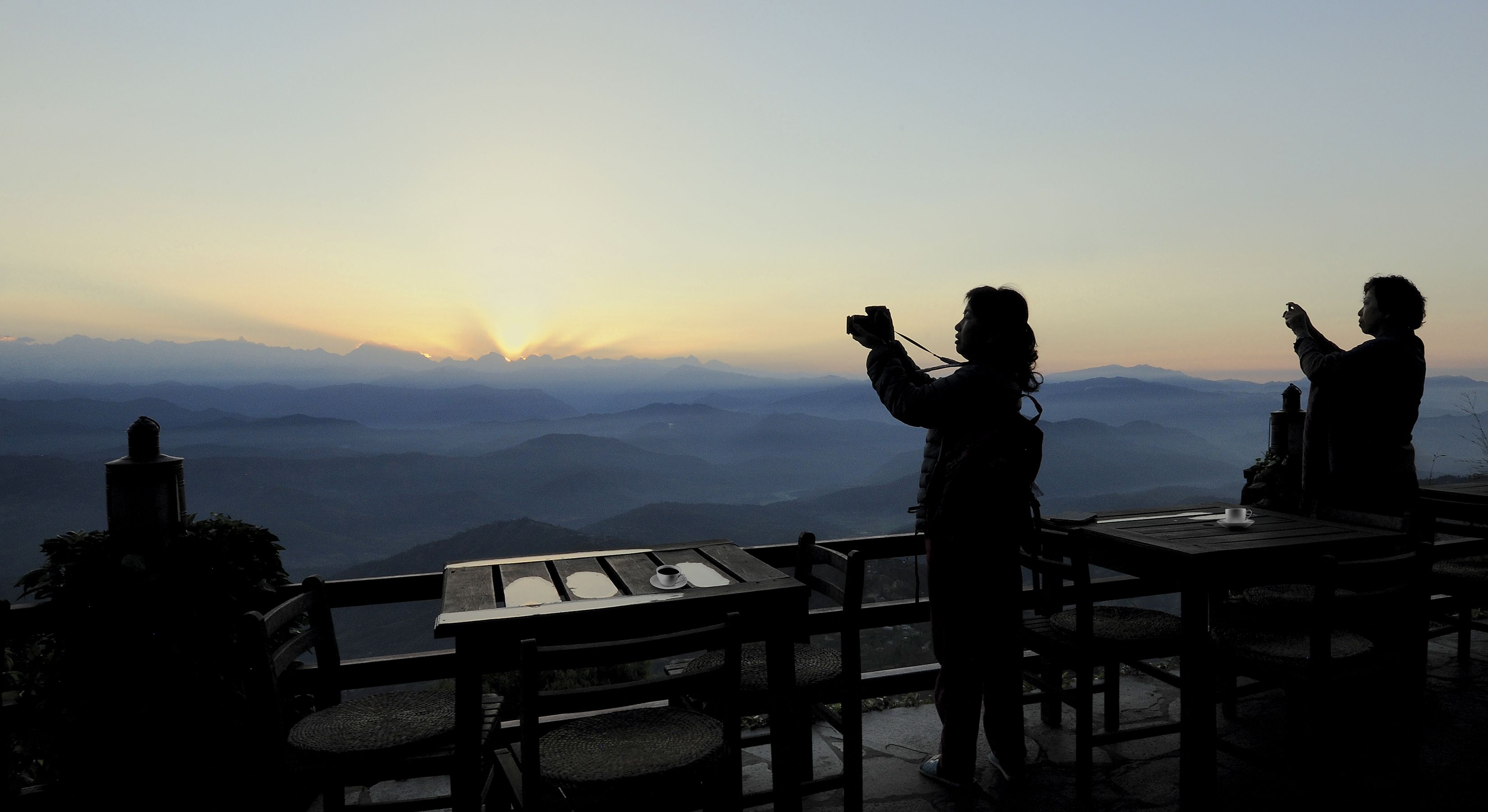 Due persone scattano foto con una vista panoramica di montagna sullo sfondo.