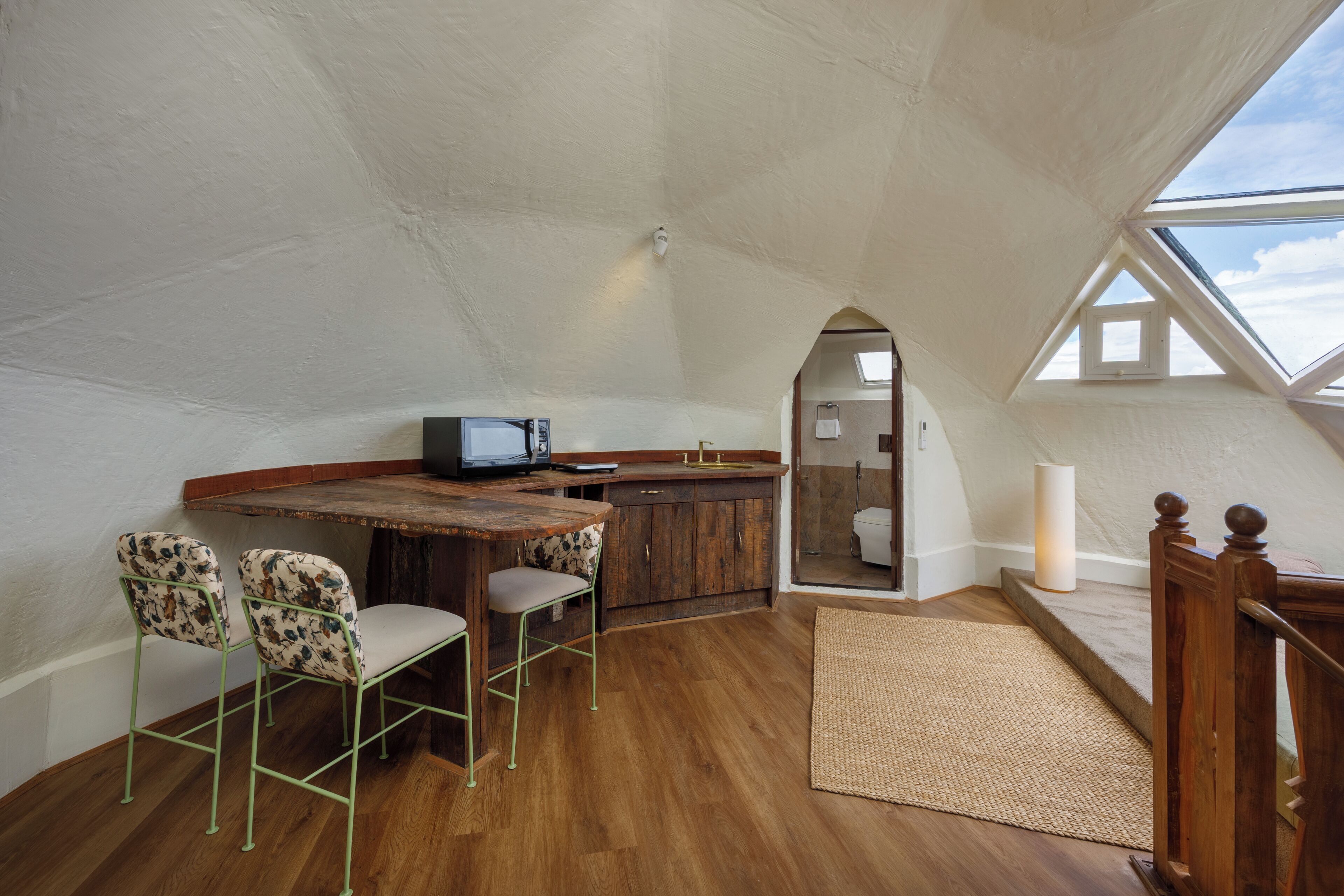 A compact, triangular room with a wooden table, two chairs, a television, and a small bathroom visible through an arched doorway.