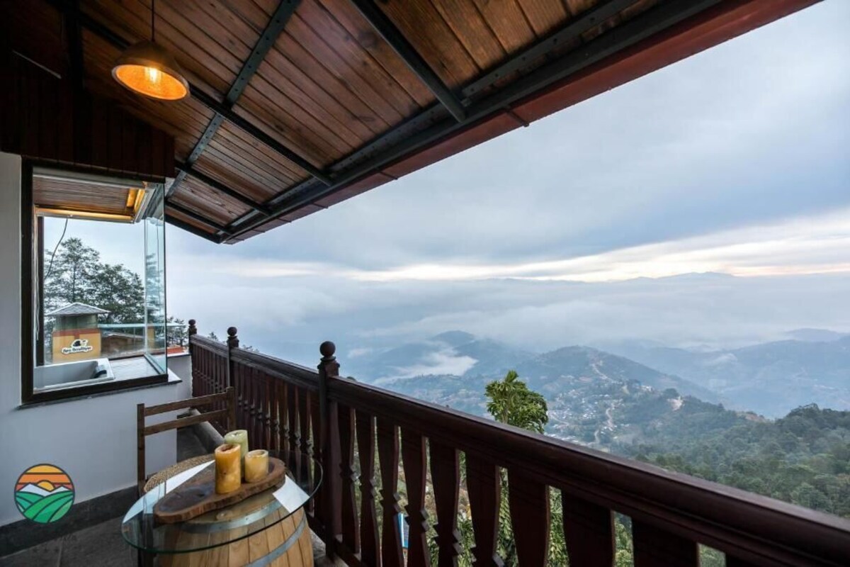 A balcony with a wooden railing, a glass table with candles, and a view of a mountainous landscape.