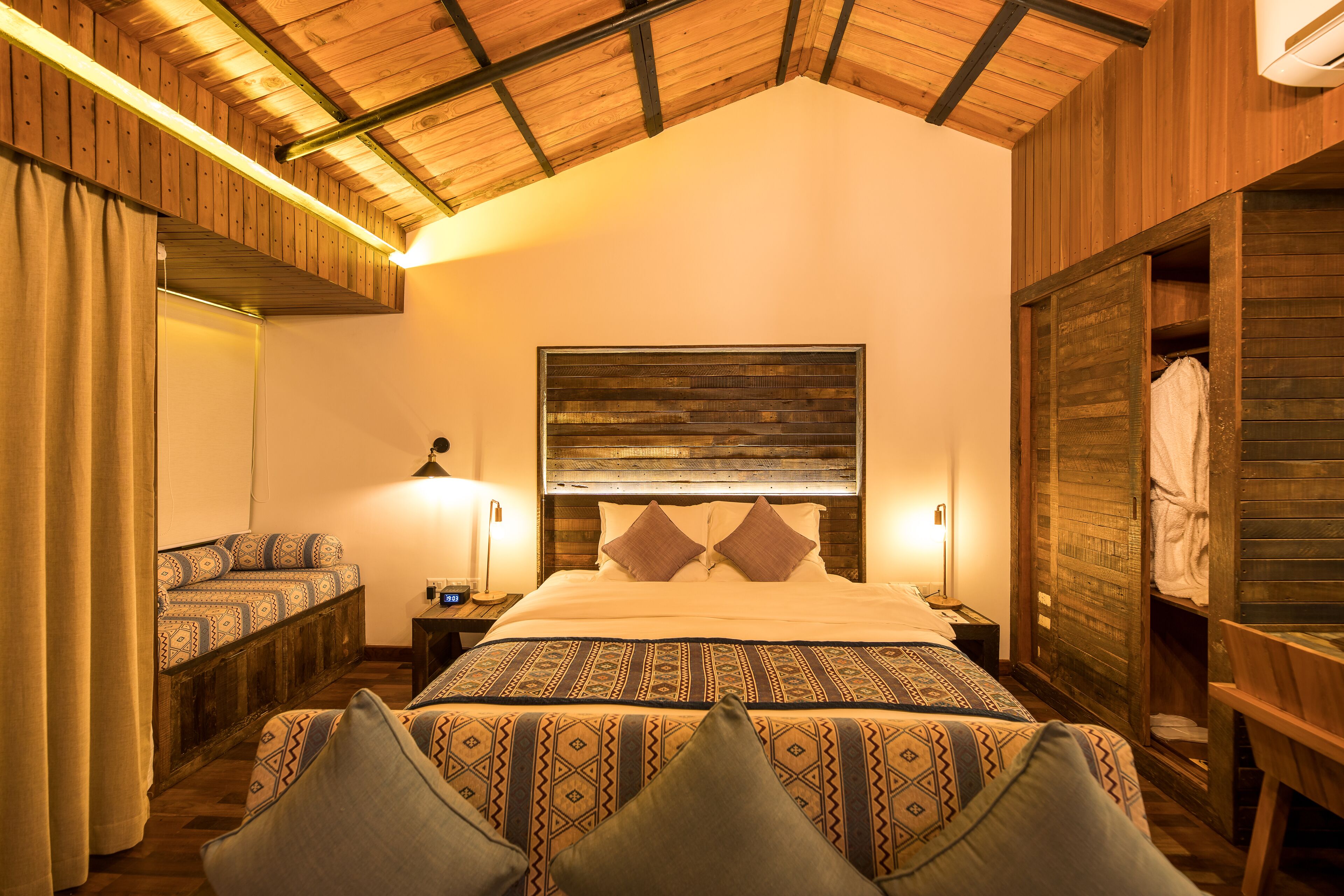 Un dormitorio con una cama grande, techo de madera, un armario y una mesita de noche con lámpara.