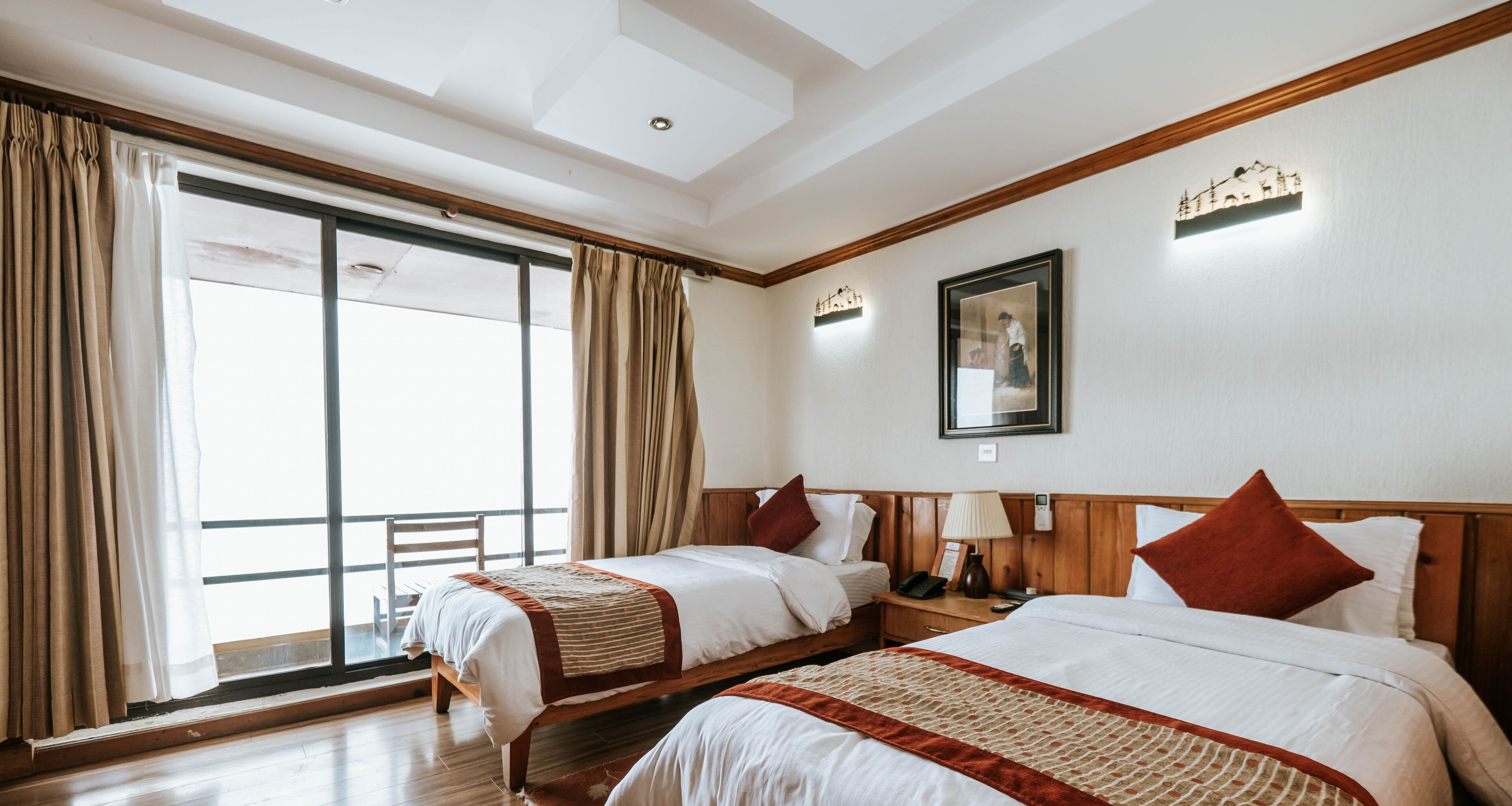 Ein Hotelzimmer mit zwei Betten, einem großen Fenster mit Vorhängen, einem Holz-Kopfteil und einem an der Wand hängenden Bild.