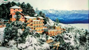 Un immeuble à plusieurs étages doté de balcons, entouré d’arbres couverts de neige et avec des montagnes en arrière-plan.