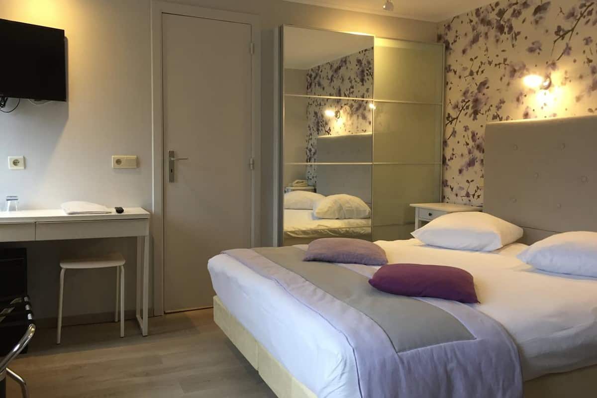 A hotel room with a bed, a desk, and a mirror.