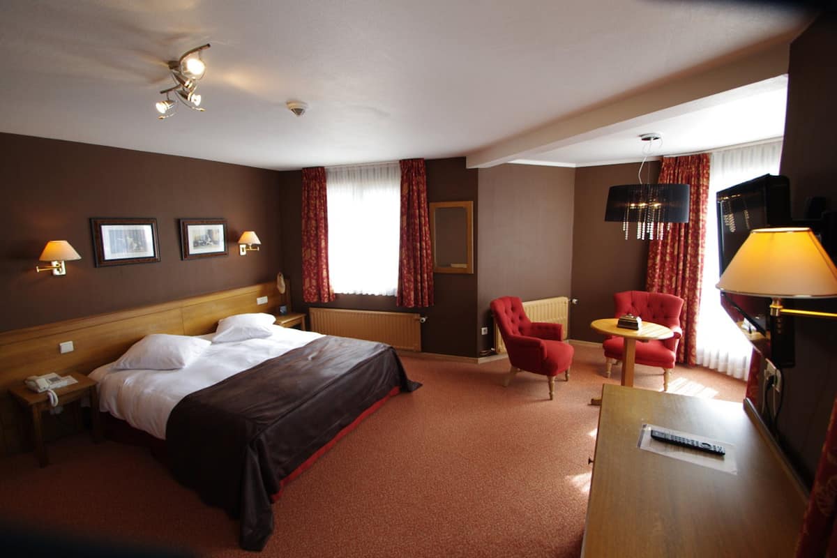 A hotel room with a large bed, a desk with a lamp, a chair, and a television.
