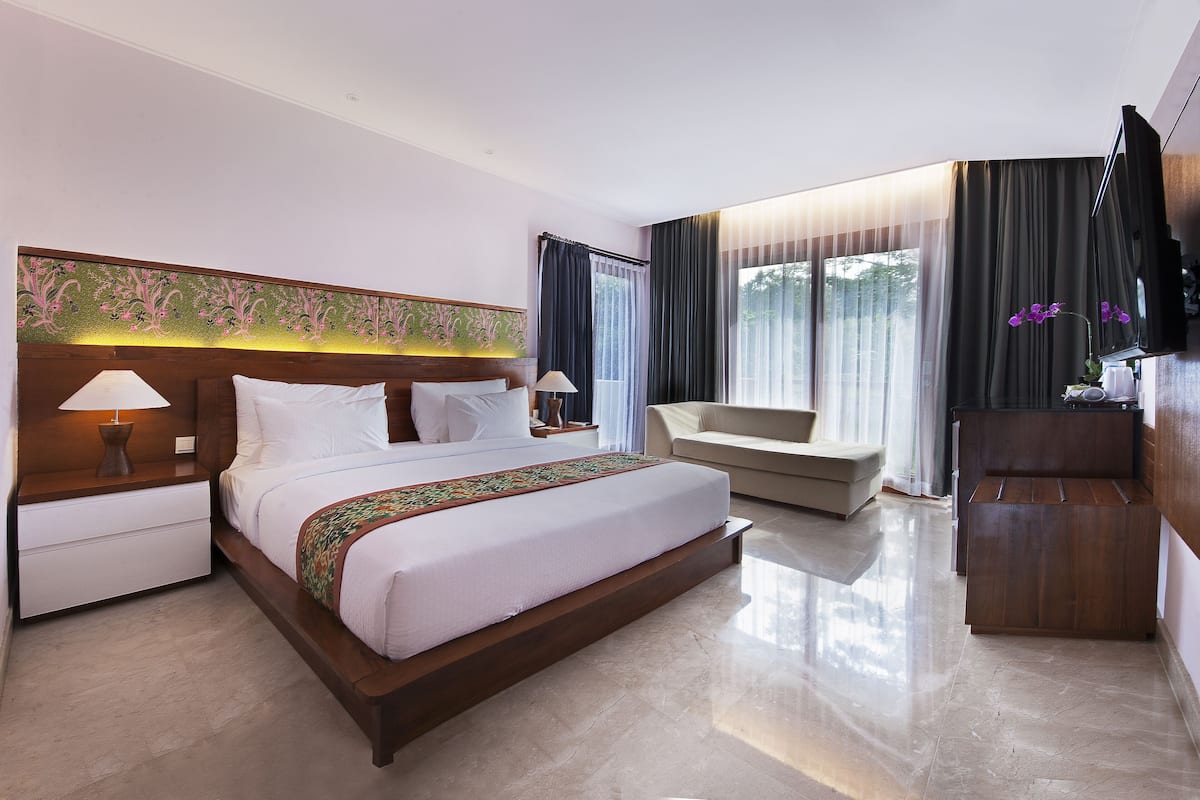 Quarto de hotel com uma cama grande, um sofá, uma TV e uma escrivaninha.