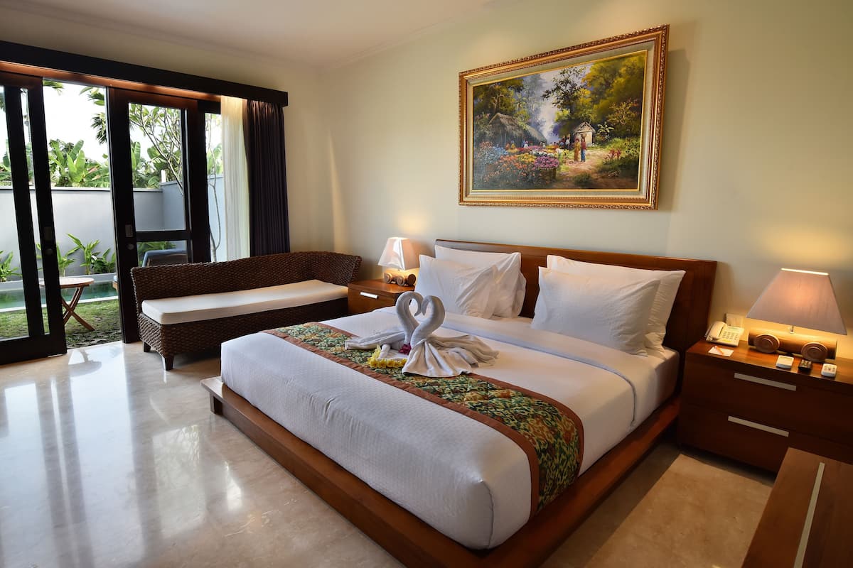Quarto de hotel com uma cama grande, uma mesa de cabeceira de madeira, uma cadeira de vime e um quadro na parede.