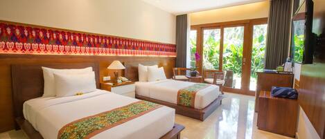 A hotel room with two beds, a desk, a chair, and a large window with a view of greenery.