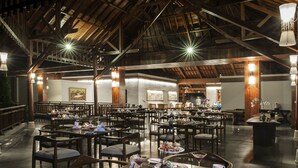 A spacious dining area with multiple tables and chairs, wooden beams on the ceiling, and artwork on the walls. - Ubud Wana Resort (Ubud)