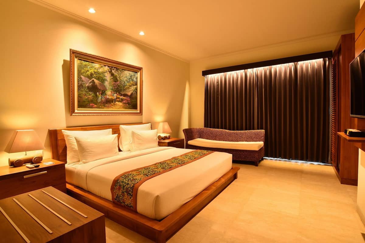 Quarto de hotel com cama, sofá, televisão, quadro na parede e janela com cortinas.