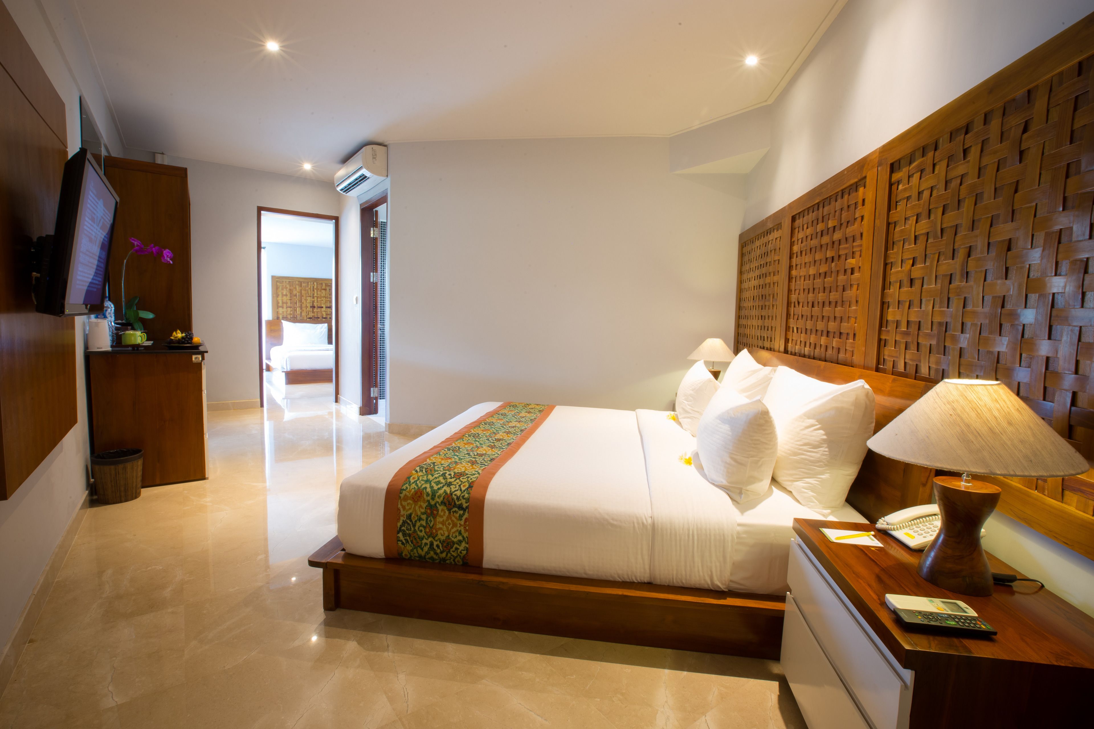 A hotel room with a large bed, a wooden headboard, a bedside table with a lamp, and a television on the wall.