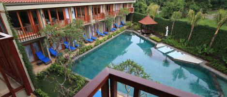 A hotel with a swimming pool, multiple balconies, and lounge chairs.