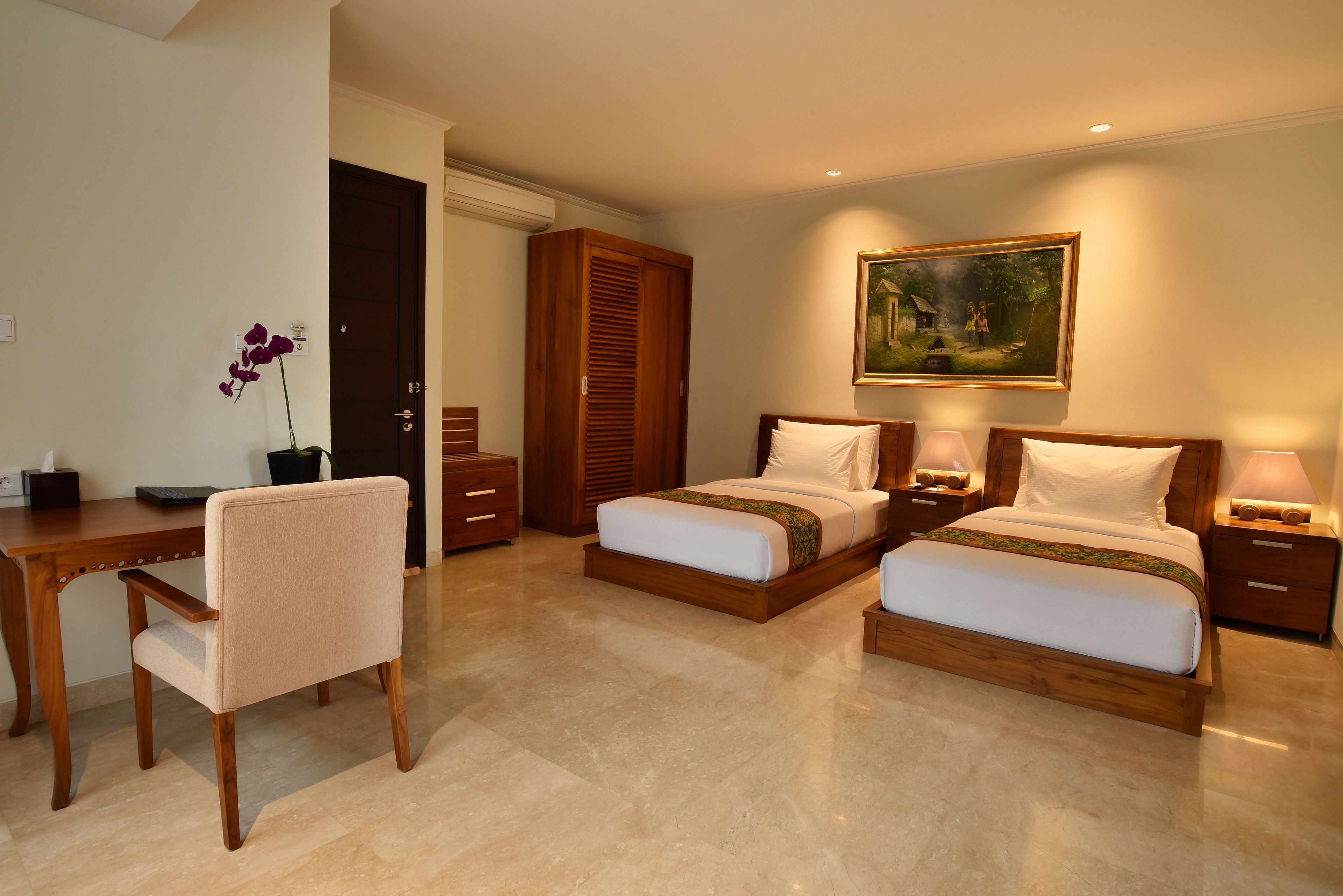 A hotel room with two beds, a desk, a chair, and a painting on the wall.
