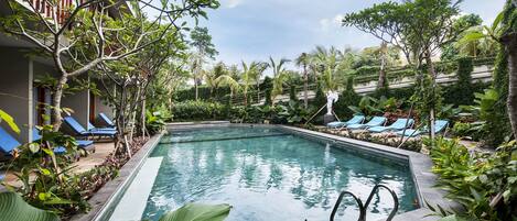 A swimming pool surrounded by lush greenery and blue lounge chairs.