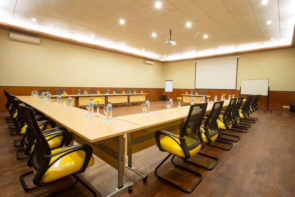 Un salón de conferencias con una mesa larga, múltiples sillas, botellas de agua y una pantalla para proyector.