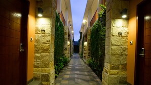 A corridor with stone walls, wooden doors, and a checkered floor leading to a building entrance. - Ubud Wana Resort (Ubud)
