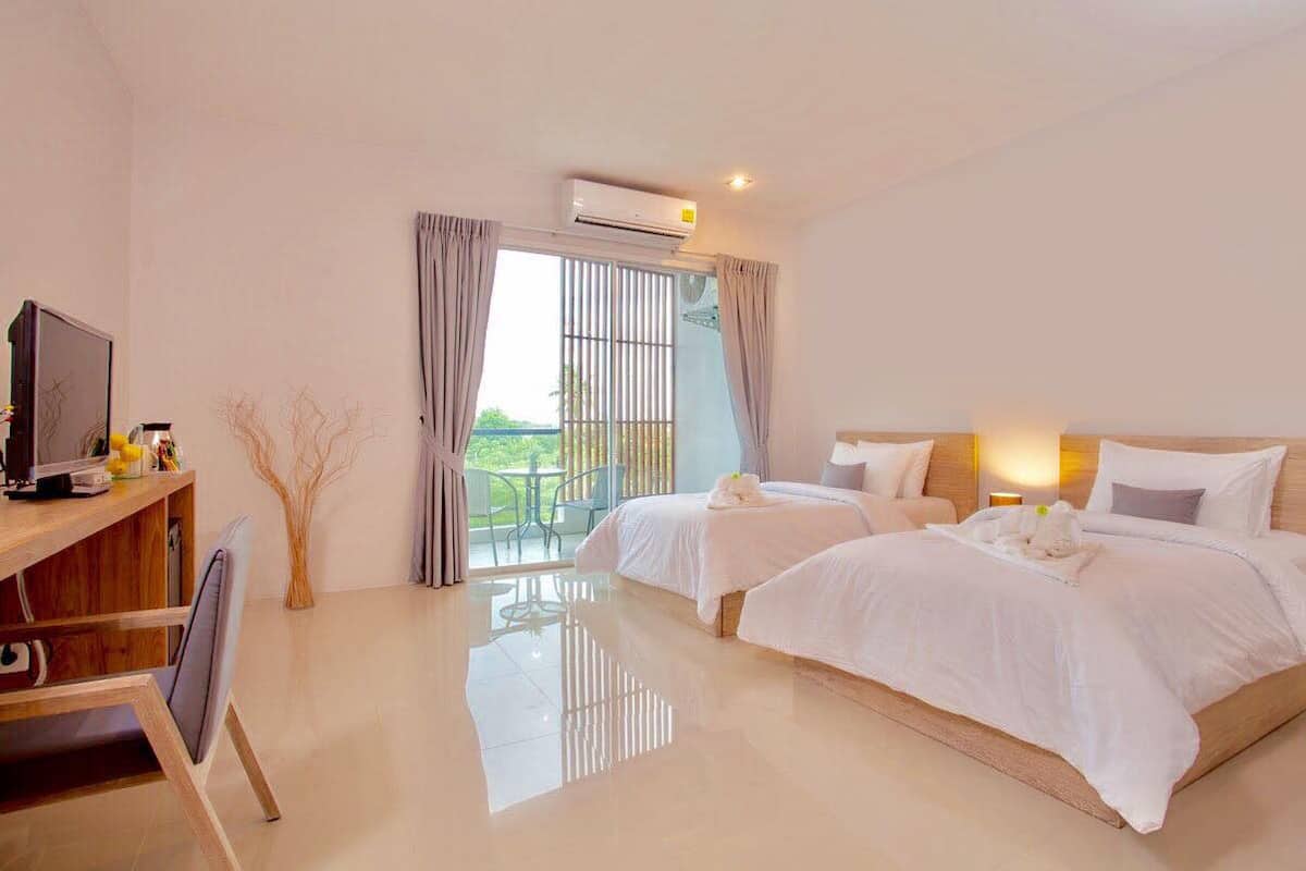 Habitación de hotel con dos camas, televisión, escritorio y balcón con cortinas.