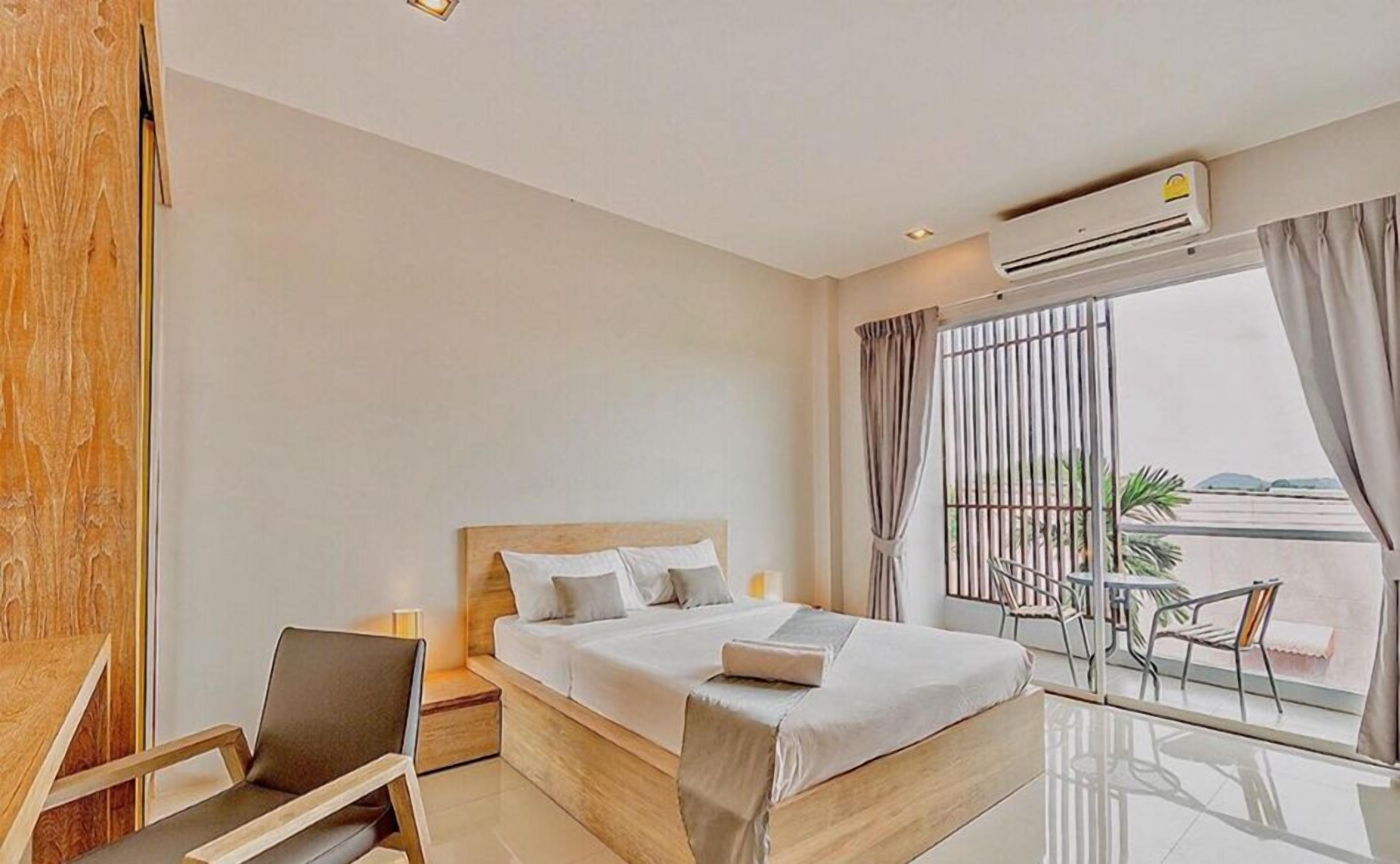 A modern hotel room with a large bed, a desk, and a balcony with a table and chairs.