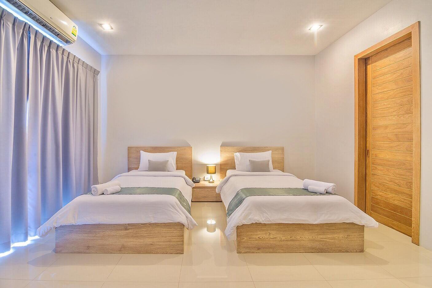 A hotel room with two wooden beds, a nightstand with a lamp, a wooden wardrobe, and a window with curtains.