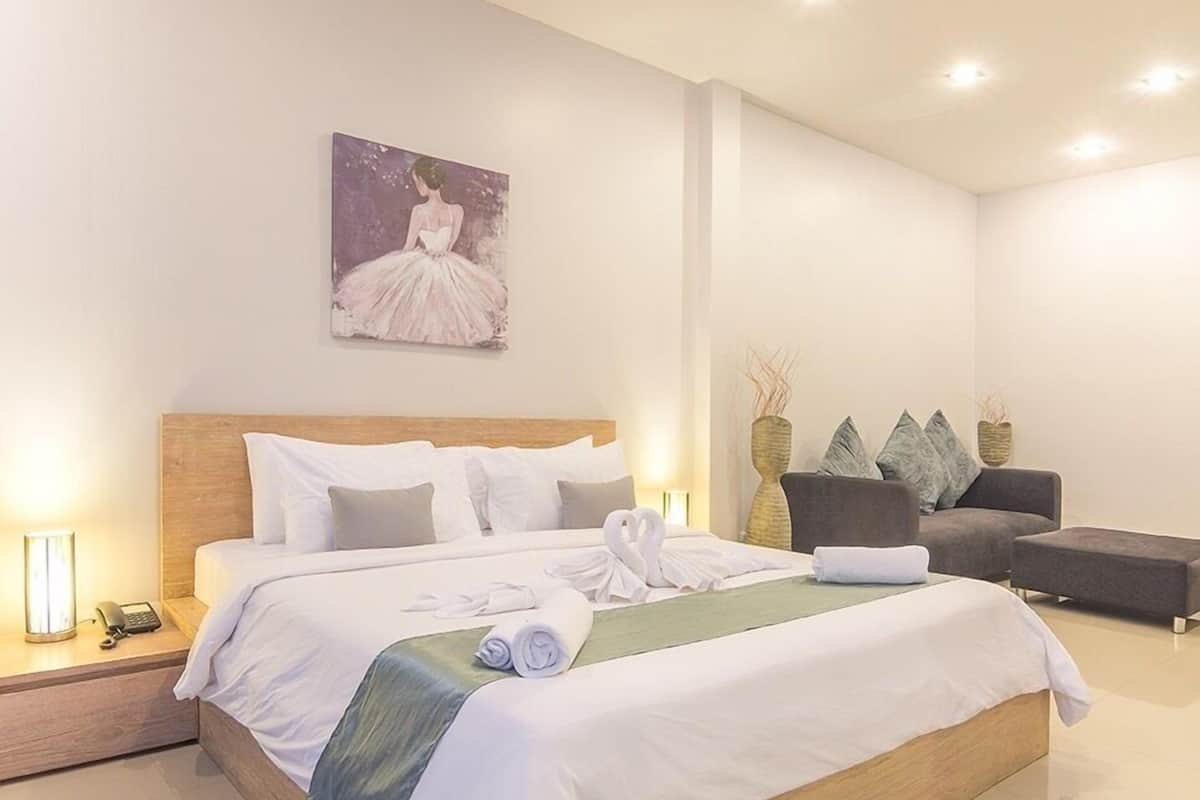 Una habitación de hotel moderna con una cama grande, mesitas de noche, un sofá y un cuadro en la pared.