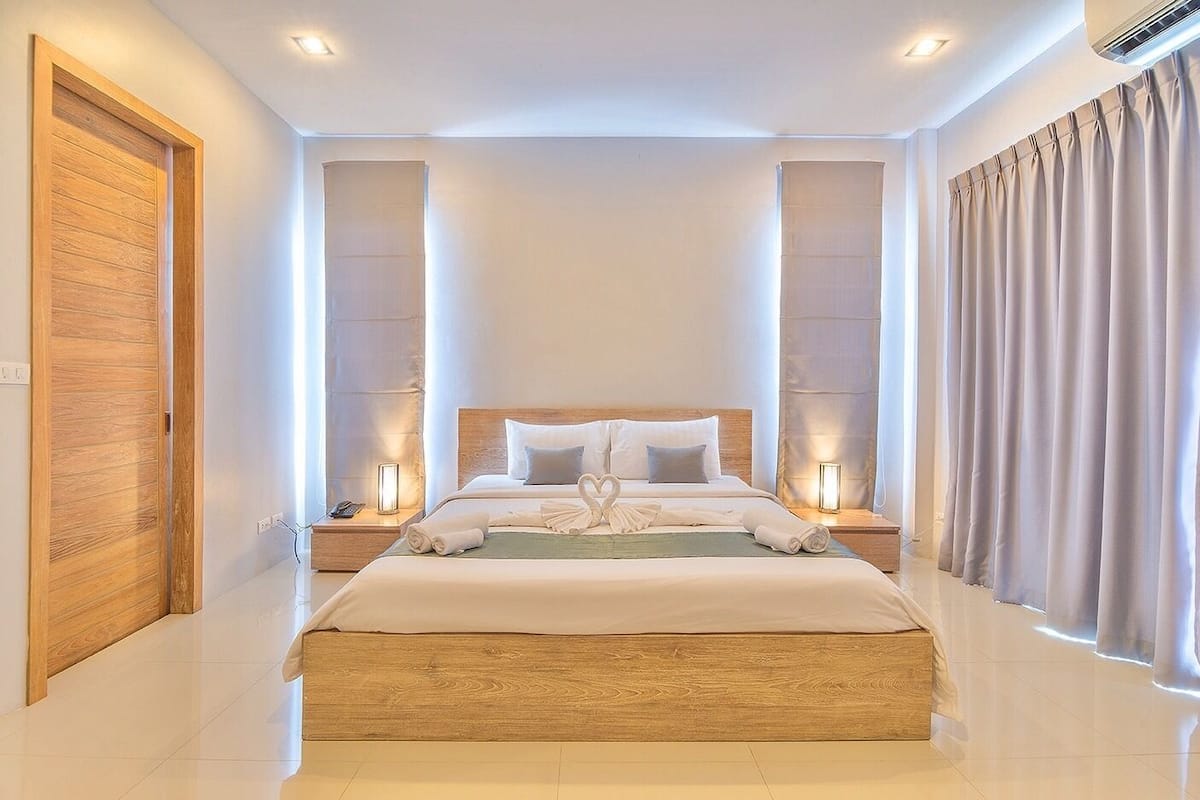 Una cama grande y central con cabecera de madera, flanqueada por dos mesitas de noche con lámparas, en una habitación de hotel moderna.