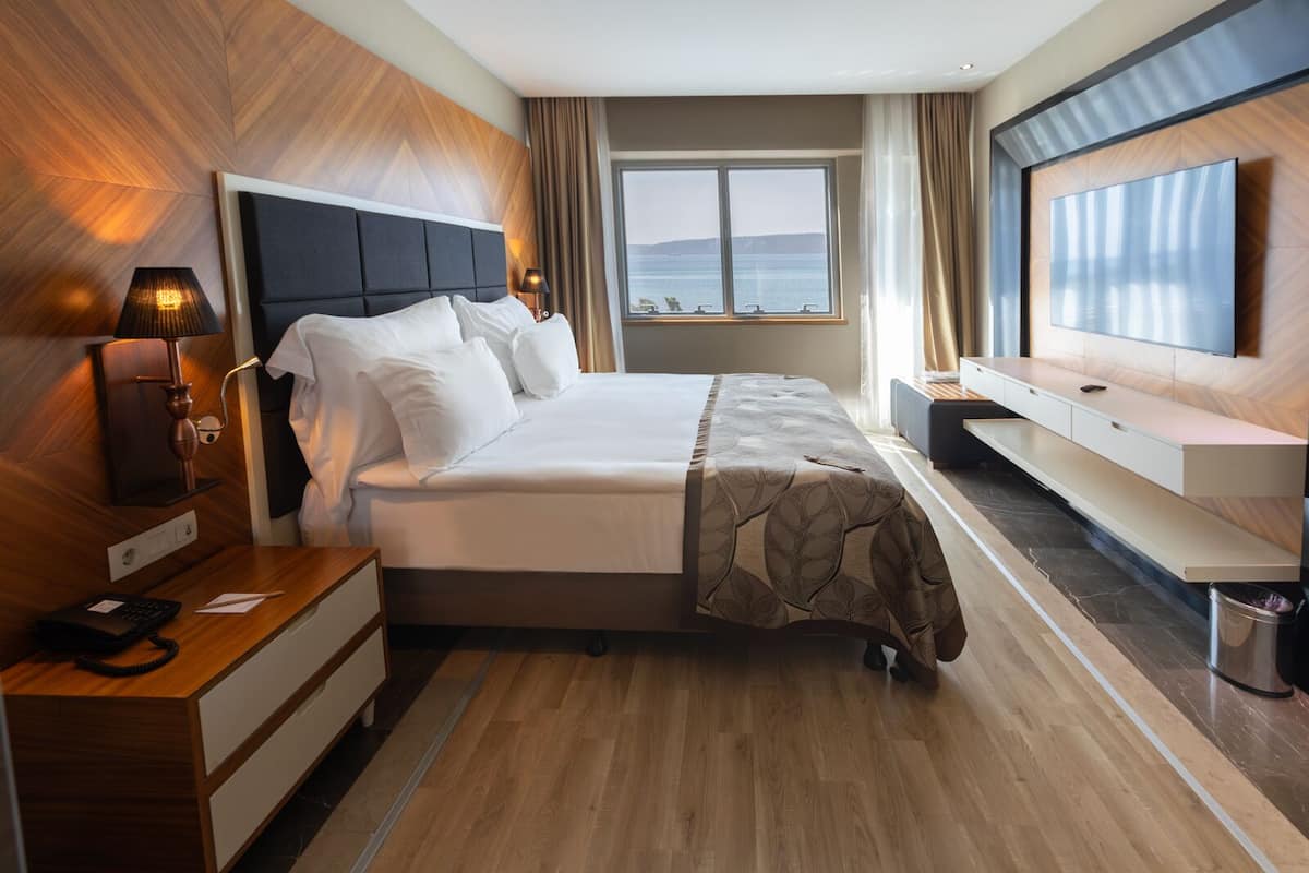 A hotel room with a bed, bedside table, lamp, and a TV mounted on the wall.