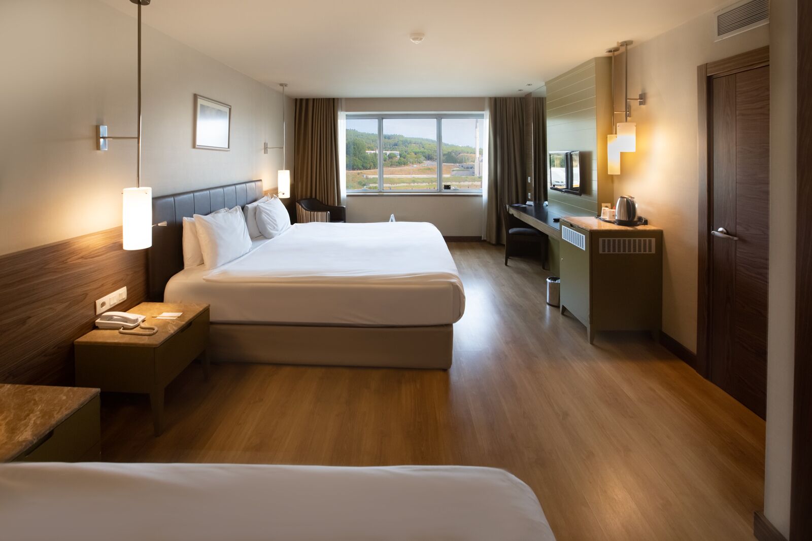 A hotel room with two beds, a desk, a chair, a telephone, and a window with a view of the landscape.
