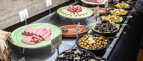 A buffet with various food options including meats, cheeses, olives, and other dishes.