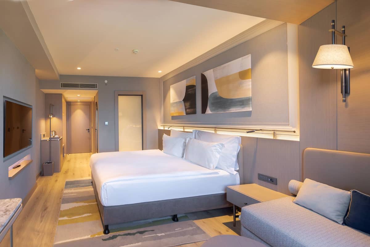A modern hotel room with a large bed, bedside tables, a TV, and artwork on the wall.