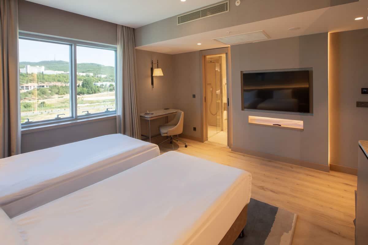 A hotel room with two beds, a desk, a TV, and a bathroom visible through an open door.