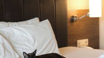 Un lit avec des draps blancs et un chat qui y est allongé.