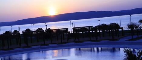 A serene pool area with a sunset view, surrounded by a structured deck and palm trees.