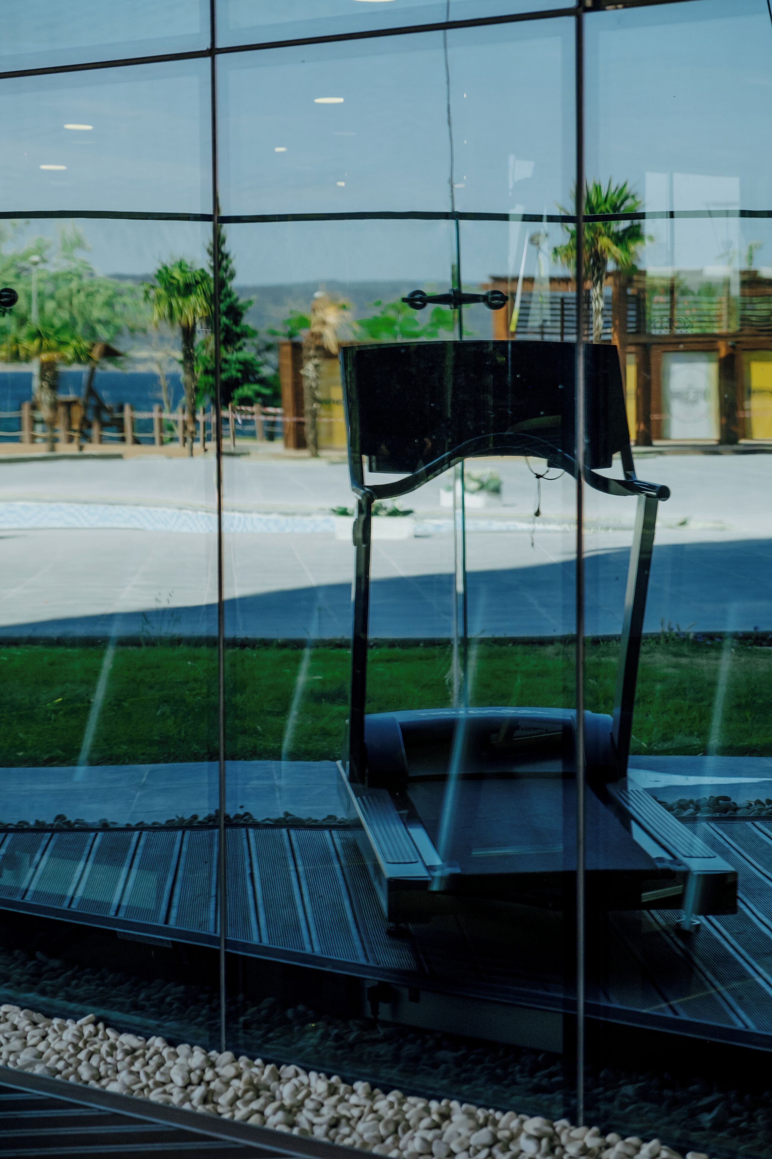 A modern building with a glass facade reflecting a bench and a pathway.
