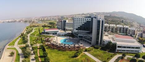 A modern hotel with a swimming pool, surrounded by well-maintained lawns and a view of the sea.