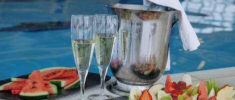 A poolside setting with a fruit platter, two glasses of champagne, and a bucket of ice.