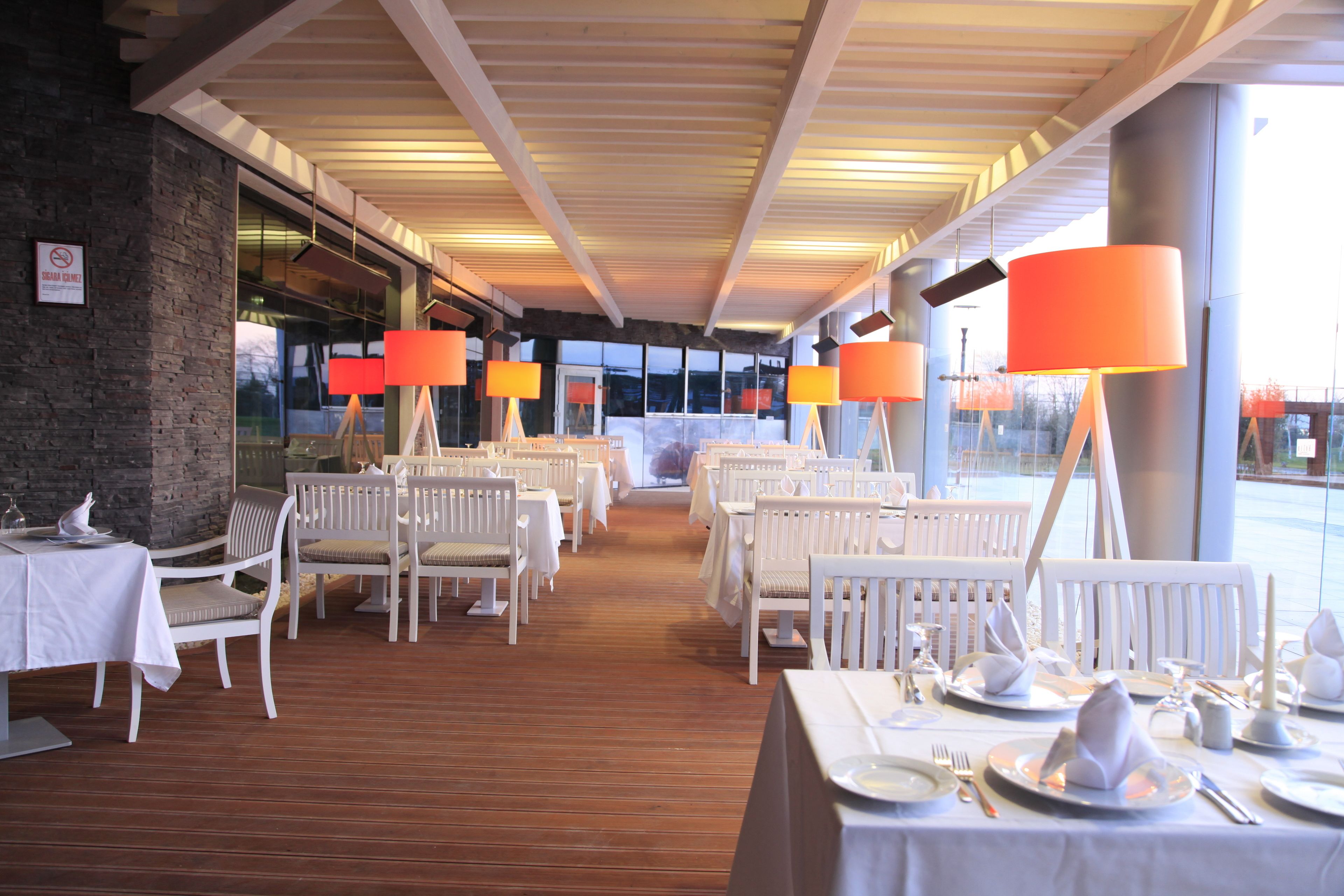 Un restaurant avec des chaises et des tables blanches, des lampes orange et un mur en briques.
