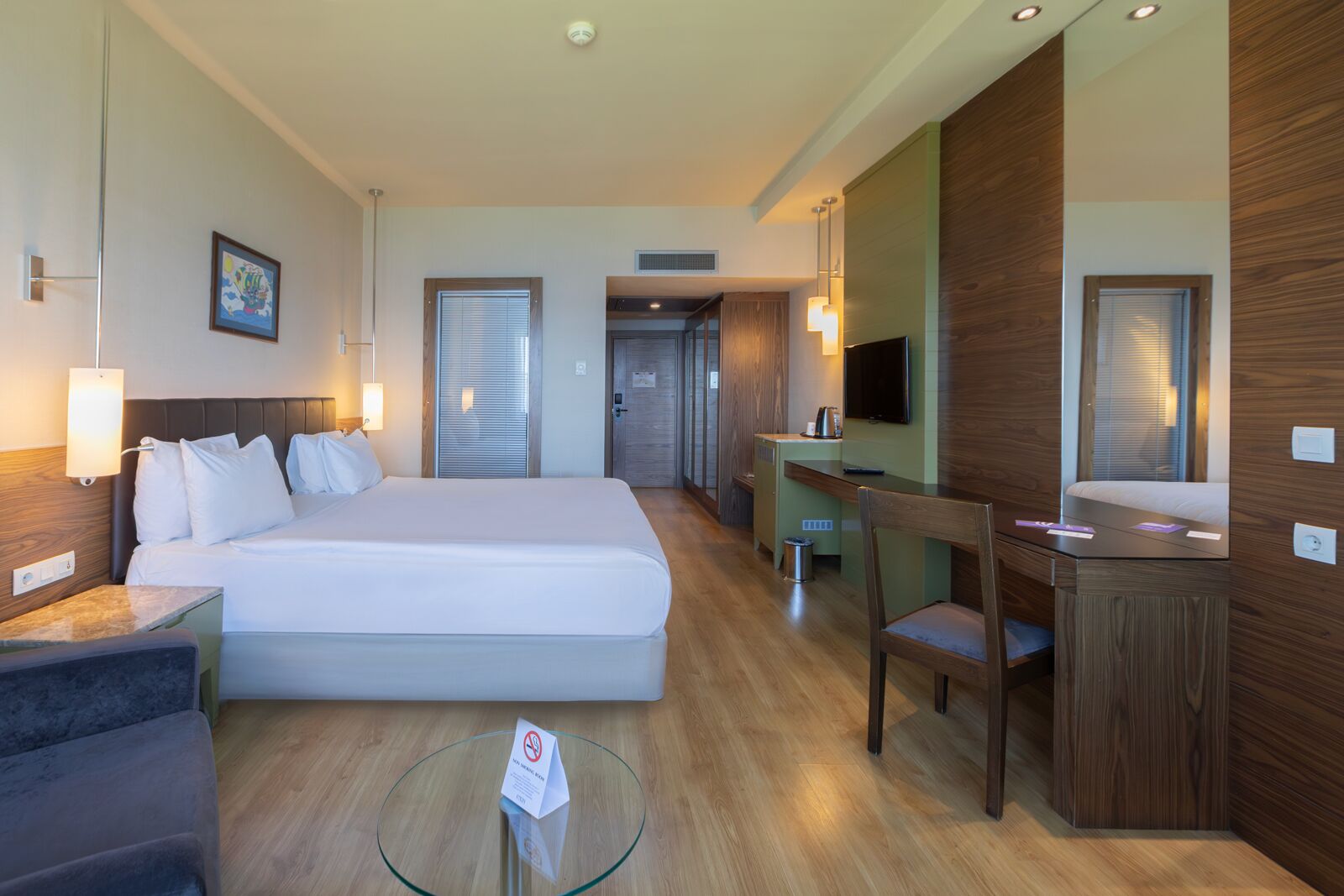 Una habitación de hotel con una cama grande, un escritorio, una silla, un televisor y una mesita con un letrero.