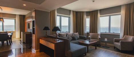 A modern hotel room with a dining area, seating arrangement, and large windows offering a view of the sea.