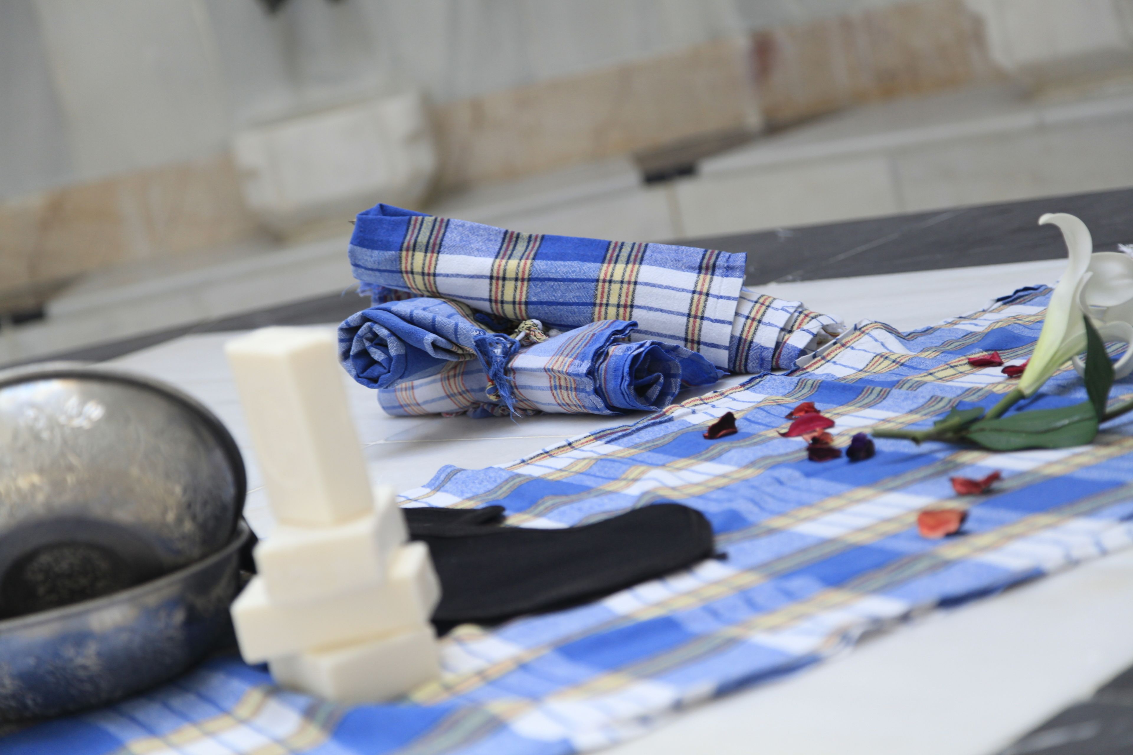 A bed with a blue and white checkered blanket, a white pillow, and a metal bowl.