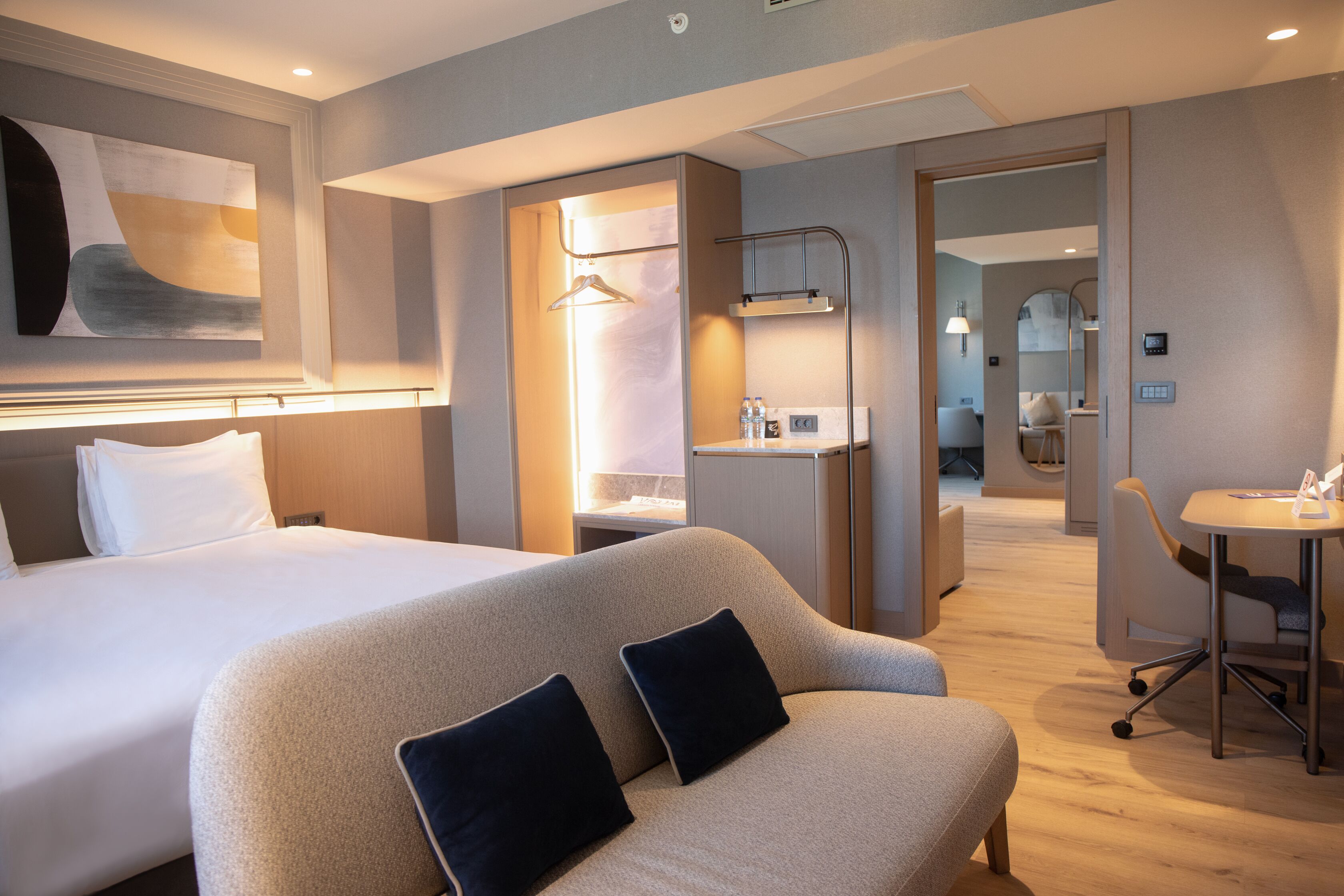 A modern hotel room with a large bed, a sofa, a desk, and a bathroom.