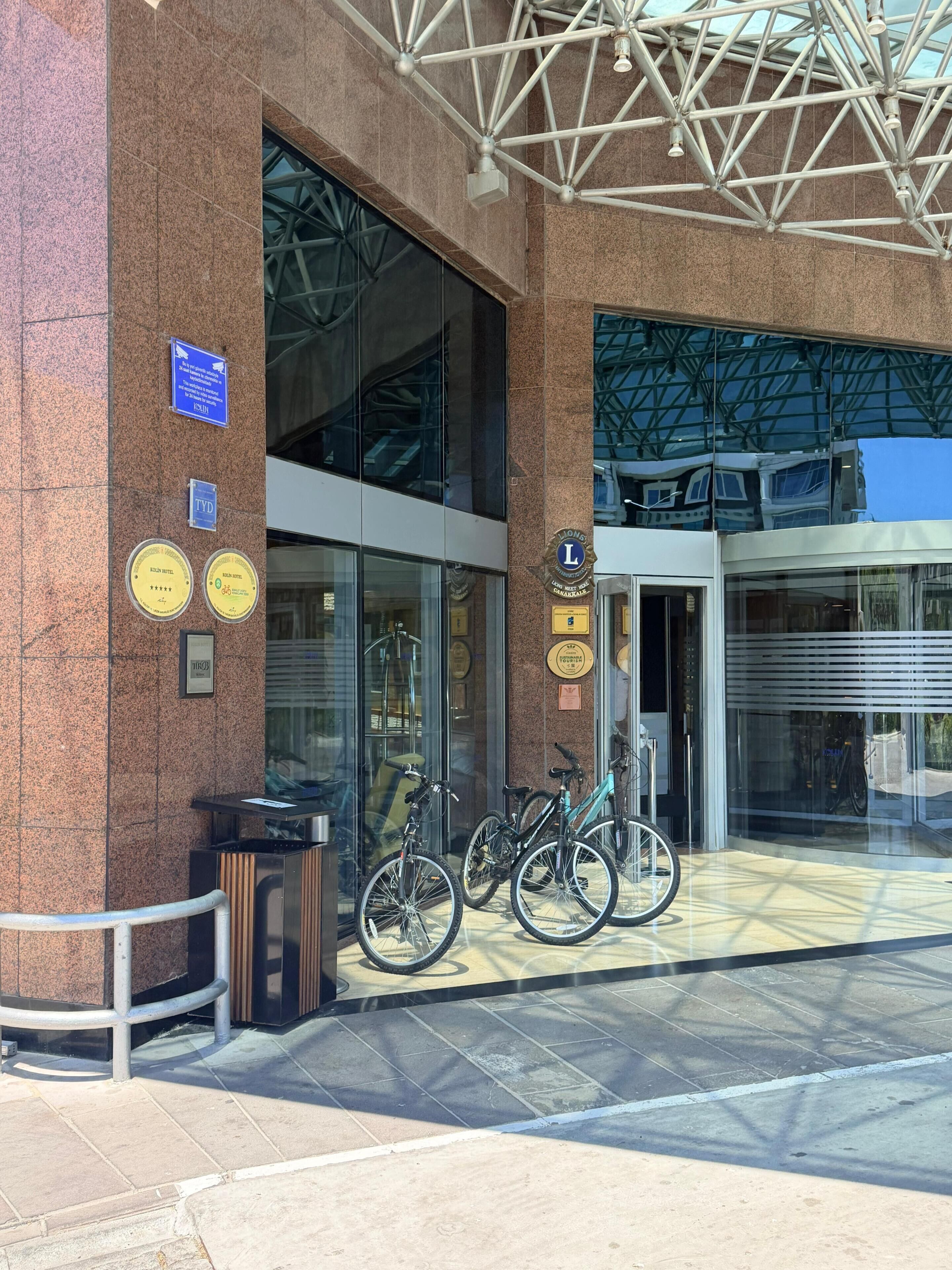 A building entrance with a glass facade, a metal roof structure, and bicycles parked outside.