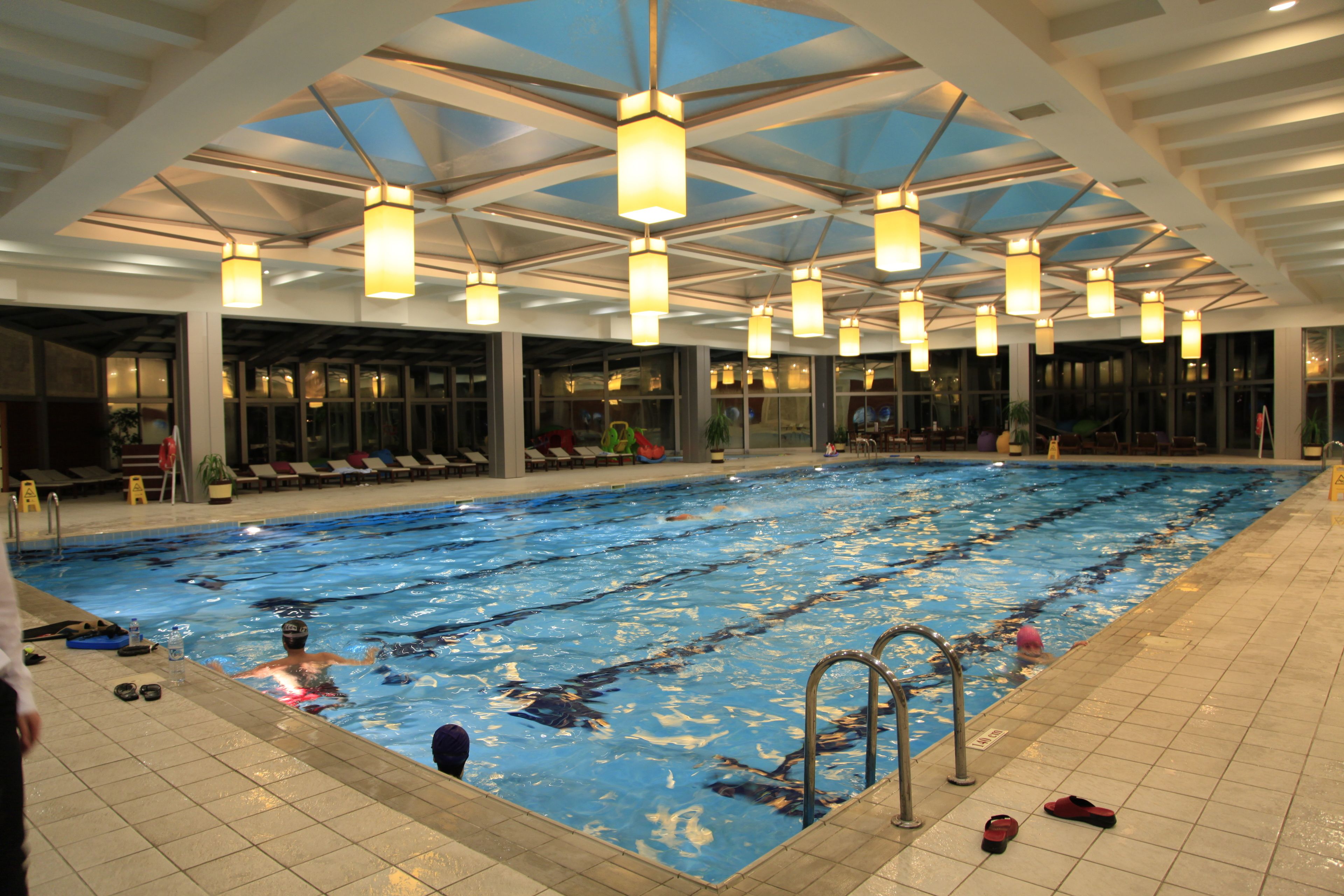 An indoor swimming pool with multiple lanes, overhead lighting, and a tiled floor.