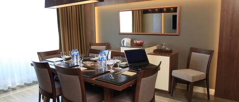 A hotel dining area with a wooden table, chairs, a laptop, and various items on the table.