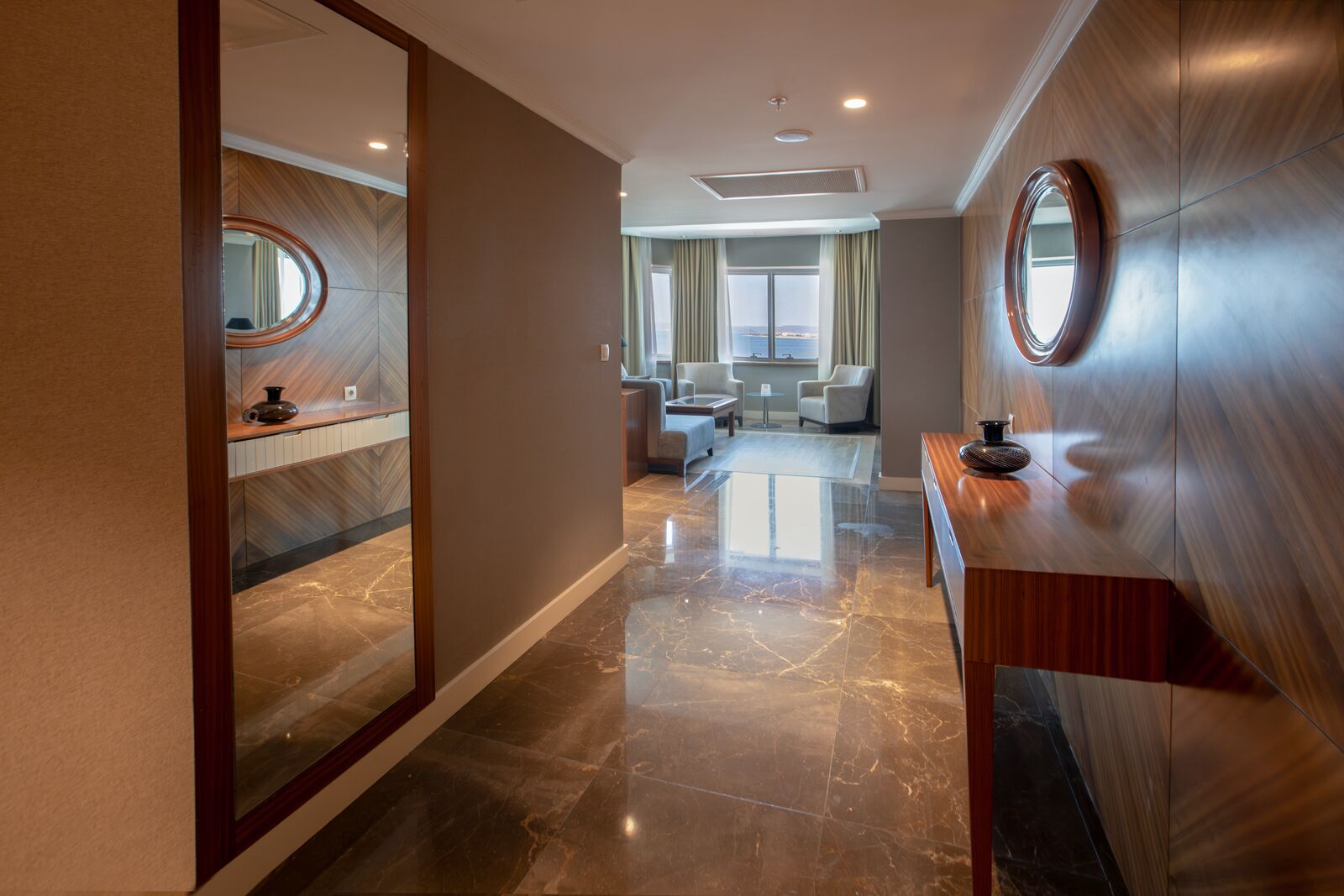 A modern hotel lobby with a marble floor, a reception desk, and a seating area with chairs and a small table.