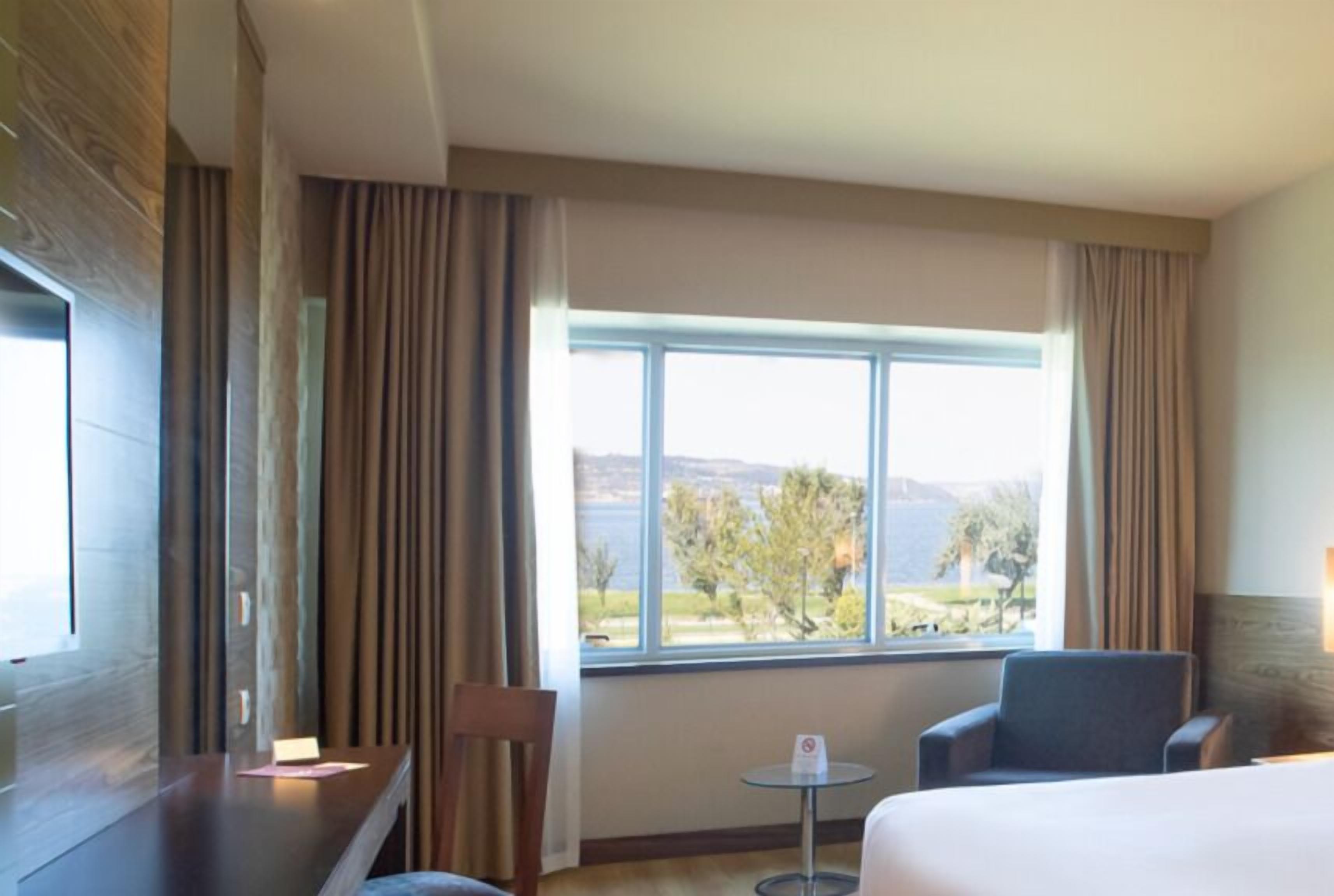 Een hotelkamer met een groot raam, een bed, een stoel en een tafeltje.