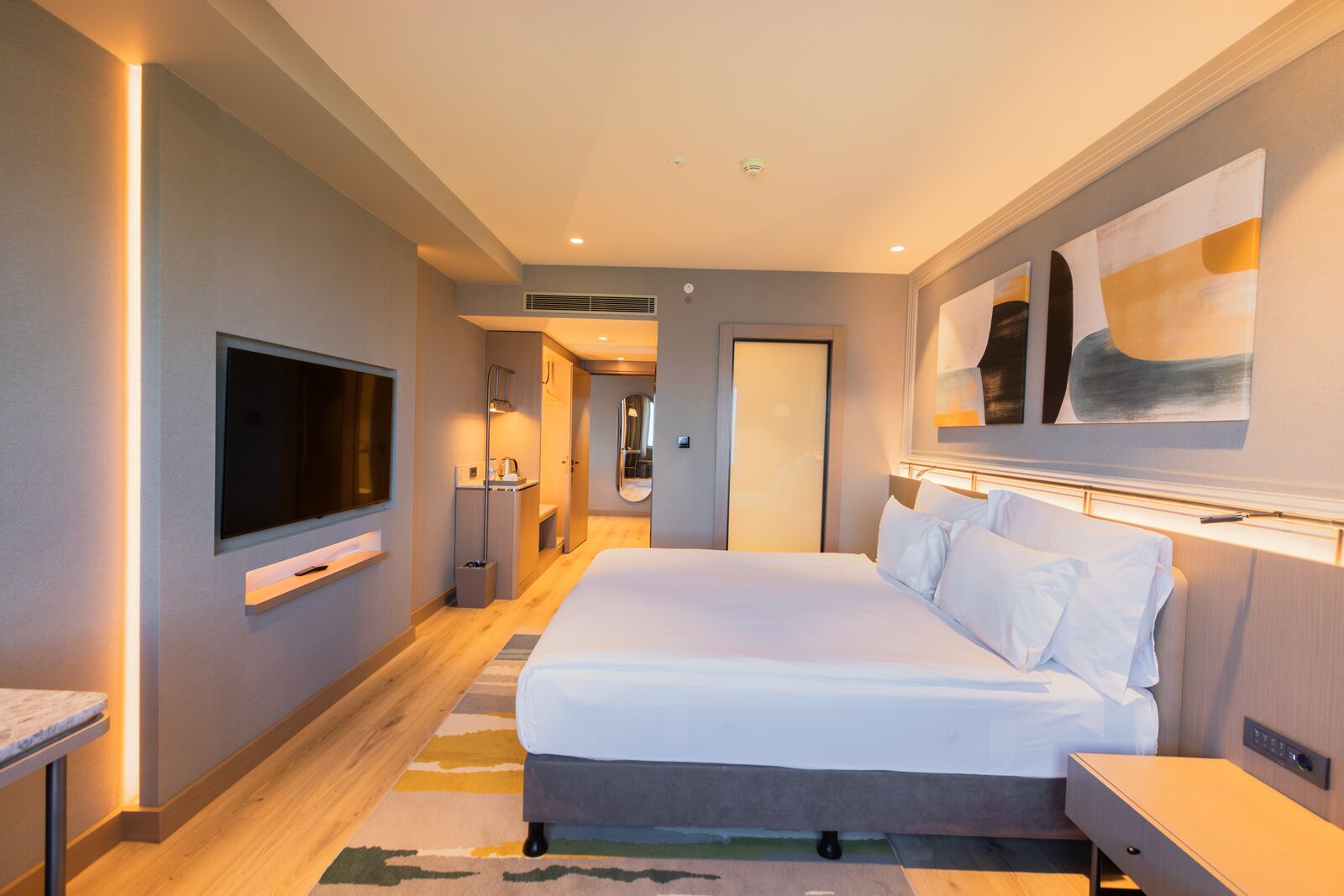 Una habitación de hotel moderna con una cama grande, un televisor de pantalla plana, una mesita de noche y una obra de arte colgada en la pared.