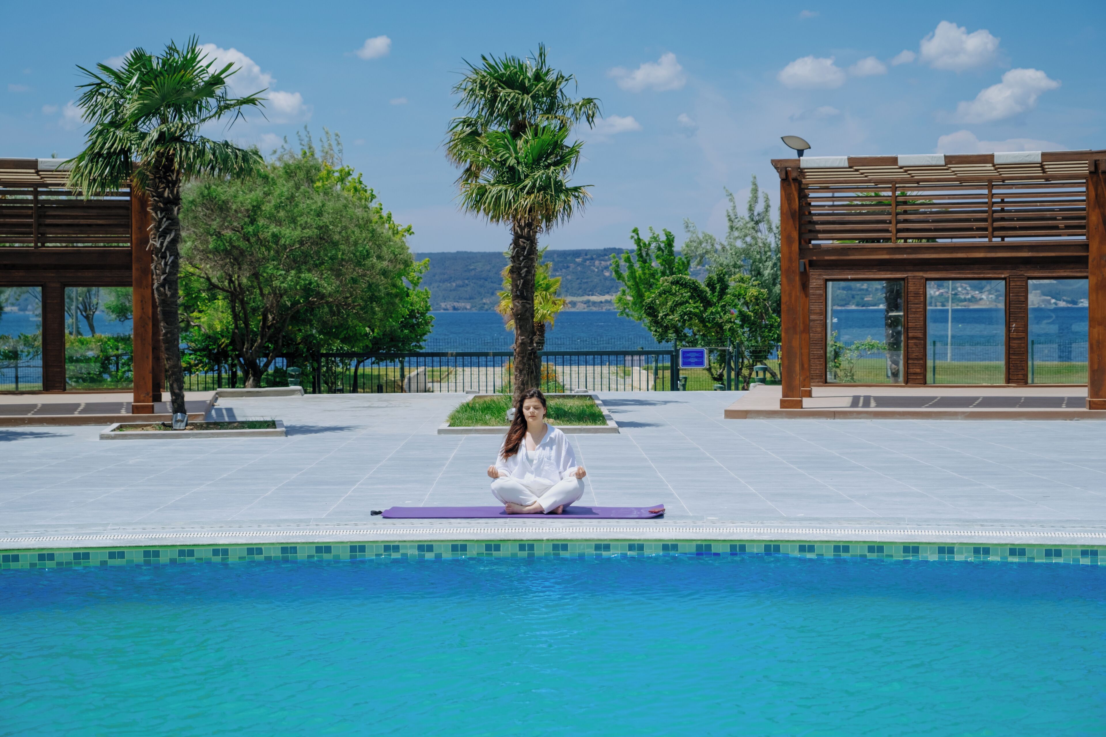 Una persona meditando junto a una piscina con vistas al mar y a las montañas.
