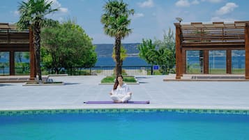 Una persona meditando junto a una piscina con vistas al mar y a las montañas.