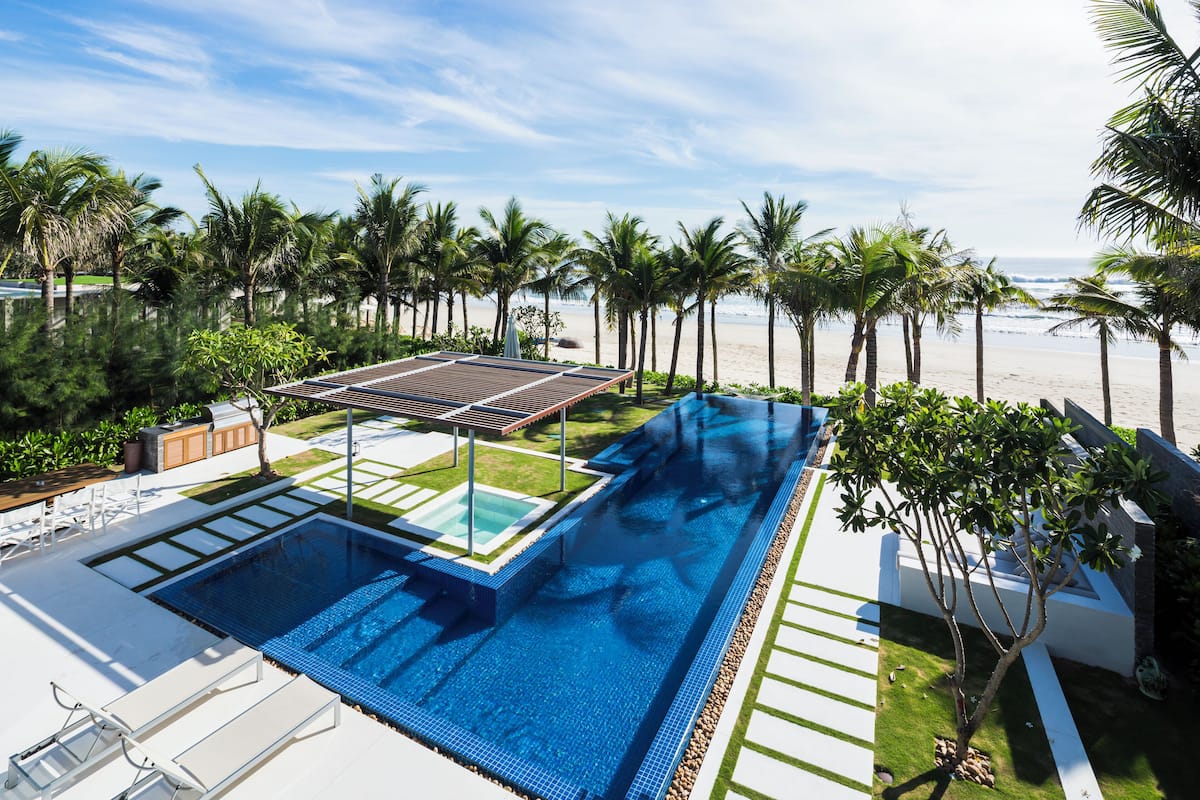 Une piscine dotée d’une terrasse ensoleillée, entourée de palmiers et offrant une vue sur la plage.