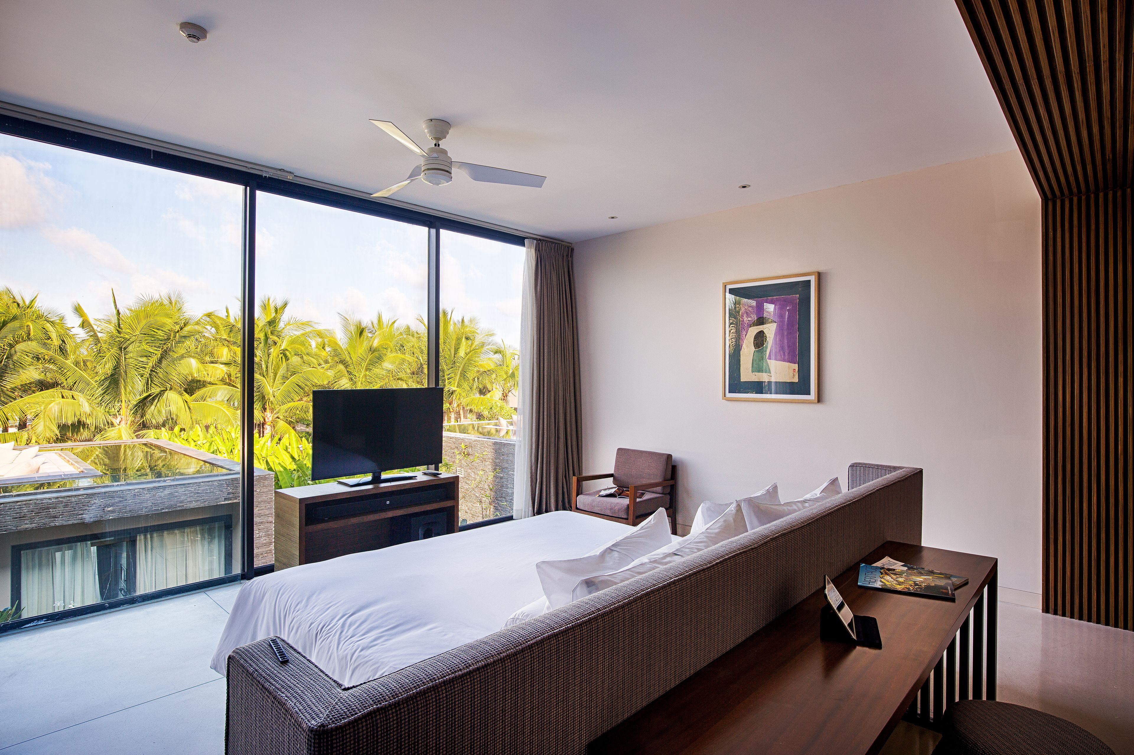 Quarto de hotel moderno com uma cama grande, televisão, cadeira e mesa com uma revista.