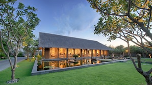 A modern house with a thatched roof, surrounded by a well-maintained lawn and a small pond.